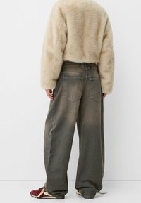 Jeans de pierna ancha color verde oliva descolorido con cintura alta, que cuentan con dos bolsillos traseros y costuras visibles, combinados con un suéter crema de tejido suave y esponjoso.