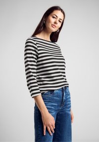 Czarna i biała bluzka w paski z rękawami 3/4, w połączeniu z niebieskimi dżinsami. Materiał wydaje się być miękki i ma luźny krój.