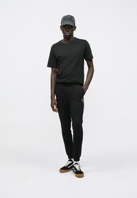 Tricou negru din bumbac, pantaloni sport negri cu talie elastică și adidași negri și albi cu talpă de gumă, completiți cu o șapcă gri.