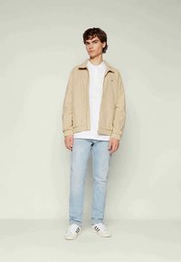Beige lightweight jacket with elastic cuffs, white T-shirt, light blue jeans, and white sneakers with black accents. Simple casual design.
