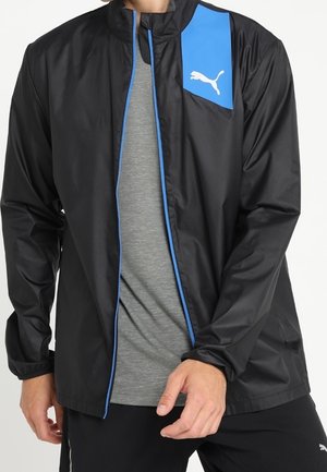 Musta kevyt takki sinisillä yksityiskohdilla, korkea kaulus, vetoketjusuljenta ja Puma-logo sinisellä paneelilla. Sileä pinta, urheilullinen muotoilu.