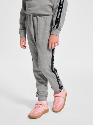 Barn iført grå joggingbukser og matchende sweatshirt med sorte "hummel" striber samt pinke sneakers med gummisåler, stående på hvid baggrund.