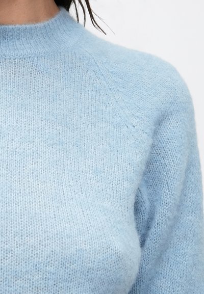 Pulover bleu deschis, tricotat, realizat dintr-un material moale și pufoasă. Are guler rotund și mâneci raglan, cu o croială ușor lejeră.