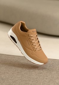Bruna sneakers med slätt läderöverdel, perforerade detaljer, rund tå, vadderad sula och vit mellansula. Varumärkeslogotyp på sidan.