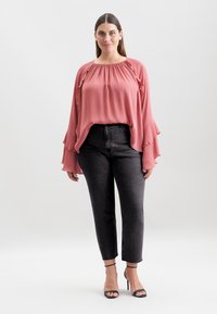 Blusa rosa lunga e con maniche a sbuffo, abbinata a jeans neri a vita alta e tacchi neri con cinturini. Tessuto morbido e leggero.