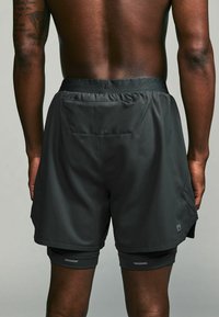 Sorte atletiske shorts med en tekstureret overflade, elastisk talje og dobbelte sidelommer. Inkluderer tætsiddende inderfor og reflekterende detaljer.