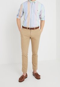 Camicia a righe multicolori con righe blu, verdi, rosa e bianche; abbinata a chinos beige e scarpe in pelle marroni.