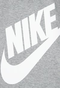 Grå bomullströja med framträdande vit "NIKE"-logotyp och swoosh-design. Slät textur med ribbat detaljer på tyget.