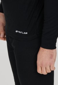 Ensemble de couche de base thermique noire en tissu côtelé, avec des manches longues et une coupe ajustée. Logo "WHISTLER" affiché en blanc.