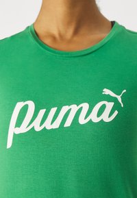 Zielona bawełniana koszulka z okrągłym dekoltem, ozdobiona wyraźnym białym logo "puma" oraz sylwetką puma, o gładkiej fakturze i klasycznym kroju.