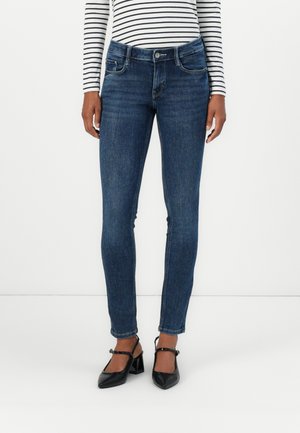 Mørkeblå denim skinny jeans med klassisk fem-lomme design, lett falming og mid-rise liv, kombinert med svarte høye hæler.