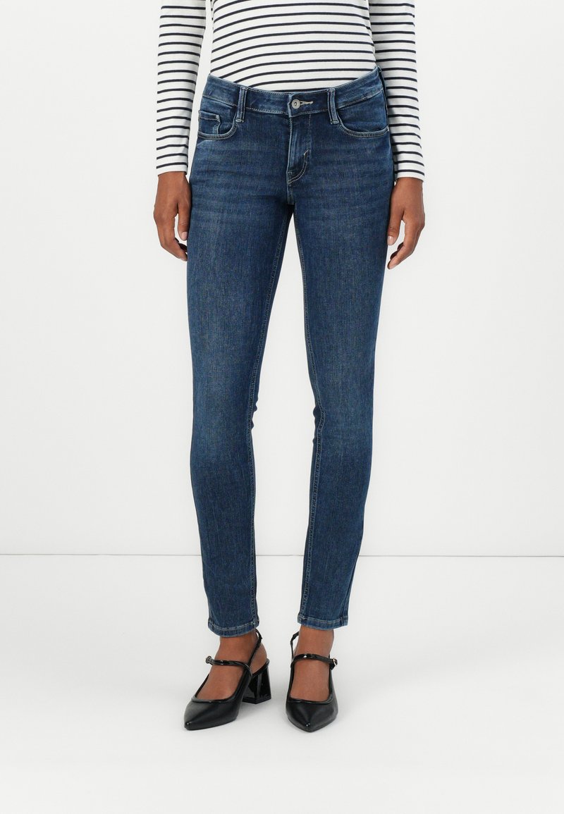 Tmavě modré džíny skinny s klasickým pětipocketním designem, mírným vyblednutím a středně vysokým pasem, doplněné černými lodičkami na vysokém podpatku.