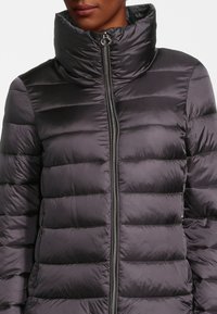 Veste matelassée en gris foncé, avec une texture côtelée et un col haut. Dotée d'une fermeture éclair avant et de poches latérales pour une fonctionnalité supplémentaire.