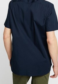 Camicia a maniche corte color navy con texture liscia e orlo arrotondato, caratterizzata da un design semplice e cuciture minime sul retro.