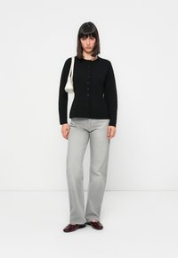Svart knapp-up cardigan, grå vide bukser, blanke burgunder sko og en liten hvit veske. Enkel, tettsittende design med en teksturert overflate.