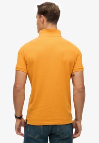 Kortærmet polo i knaldorange med tekstureret stof og klassisk krave. Simpelt design bagpå uden synlige logoer.