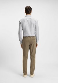 Camicia a righe azzurro chiaro con maniche lunghe, abbinata a pantaloni kaki. Scarpe casual completano l'outfit. Sfondo neutro.