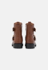 Bottes basses en cuir marron avec deux boucles latérales, une finition texturée et une semelle en caoutchouc noire robuste, avec une fermeture éclair à l'arrière.