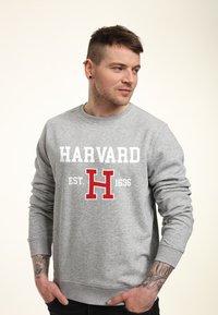 Grauer Sweatshirt mit Rundhalsausschnitt, auf dem der Text "HARVARD EST. 1636" in Weiß und Rot steht. Lange Ärmel und ribbelte Bündchen.