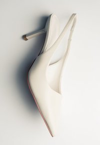Chaussure blanche en cuir à talon haut avec bride arrière, bout pointu et talon fin, photographiée sur un fond clair uni.