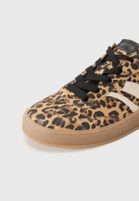 Sneakers med leopardmønster, teksturert semsket skinn på overflaten, svarte snører og gummisåle. Har en kontrasterende hvit aksentstripe.