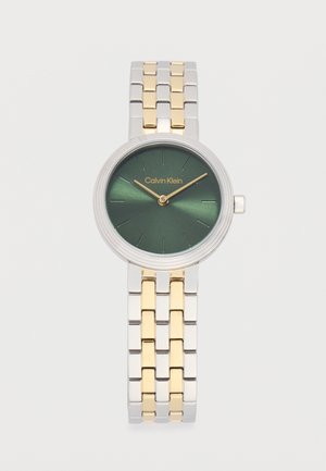 Okrugli srebrni i zlatni metalni ručni sat sa zelenim brojčanikom, zlatnim kazaljkama, minimalnim oznakama sati i logotipom Calvin Klein na poziciji 12 sati.