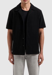 Zwart poloshirt met korte mouwen van textiel met structuur, voorzien van een puntige kraag en knoopsluiting, gecombineerd met lichtgrijze jeans.