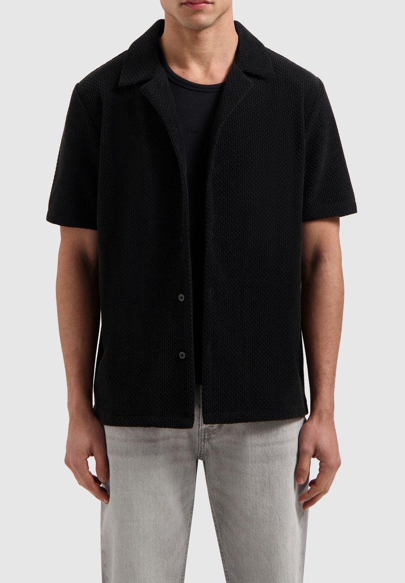 Zwart poloshirt met korte mouwen van textiel met structuur, voorzien van een puntige kraag en knoopsluiting, gecombineerd met lichtgrijze jeans.