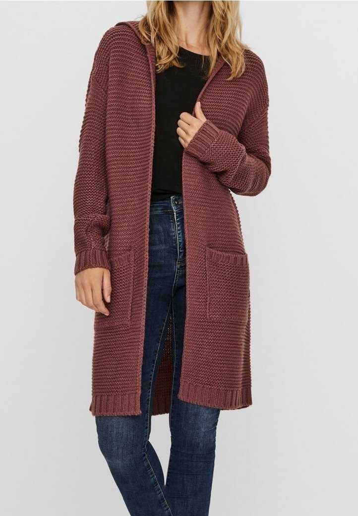 Długi kardigan z kapturem w kolorze pudrowego różu, wykonany z dzianiny, z otwartym przodem, prążkowanymi mankietami i dolną krawędzią, z dwoma przednimi kieszeniami. Połączony z czarnym topem.