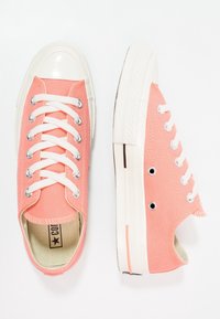 Różowe kanwowe trampki z białą gumową czubką, metalowymi oczkami i białymi sznurowadłami. Teksturowana powierzchnia z kontrastującą podeszwą i przeszyciem.