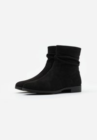 Bottines noires en daim souple avec un design flou. Elles disposent d'un petit talon empilé et d'une semelle en caoutchouc lisse. Pas de détails en métal visibles.