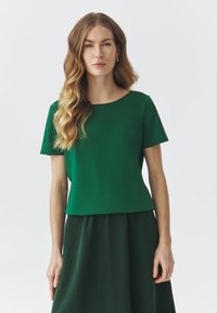 Grünes kurzärmliges Bluse mit rundem Ausschnitt, glatter Textur und lässiger Passform, getragen mit einem passenden grünen Rock.