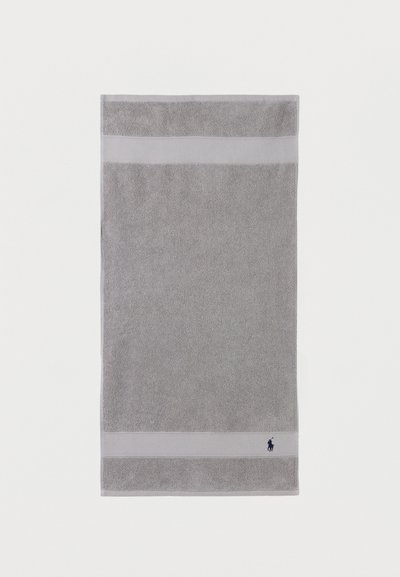 Γκρι ορθογώνια πετσέτα μπάνιου με δύο πιο ανοιχτές οριζόντιες ρίγες κοντά στις άκρες και μικρό σκούρο κεντημένο λογότυπο στην κάτω δεξιά γωνία.