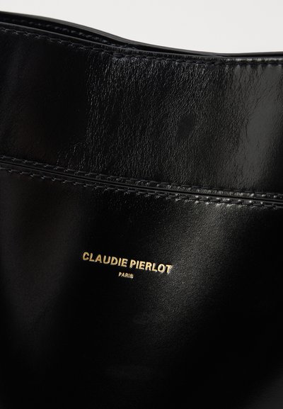 Mustapohjainen nahkakassi kiiltävällä pinnalla, jossa on yksityiskohtaiset tikkaukset ja kultainen logo, jossa lukee "CLAUDIE PIERLOT PARIS." Liukaspintainen.