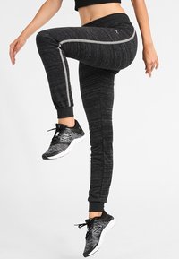 Czarne sportowe spodnie dresowe wykonane z teksturowanej tkaniny, z bocznymi paskami, przylegającymi mankietami i wysokim pasem. Dobierz do nich czarne sneakersy.