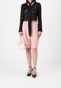 Černý průhledný top s dlouhými rukávy a květinovým vzorem, doplněný růžovými šortkami na míru. Černé vysoké podpatky a růžová kabelka.