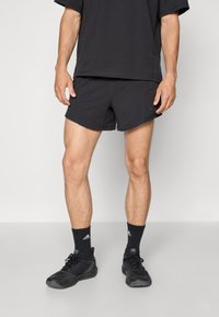 Shorts de sport noirs avec une texture lisse, présentant un design simple et des coutures latérales. Associés à des chaussettes montantes noires et des chaussures de sport.