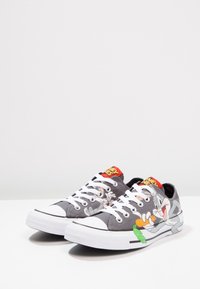 Sneakers in tela grigia con suole in gomma bianca. Presentano una grafica di Bugs Bunny, lacci bianchi e dettagli rossi sulla linguetta.