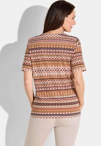 T-shirt à manches courtes à motifs présentant des rayures horizontales dans des tons terreux, avec des designs floraux et géométriques en rouge, crème et marron.