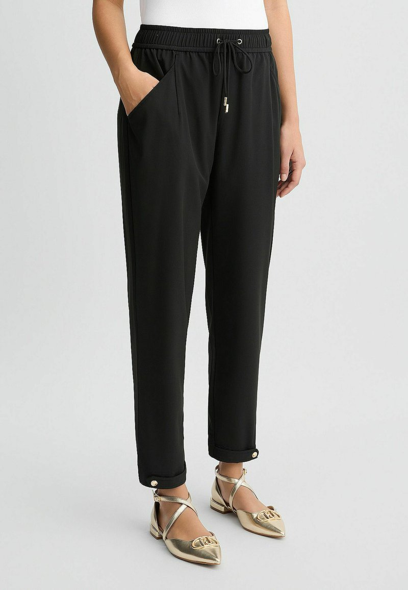 Schwarze, taillierte Hosen mit elastischem Bund, Seitentaschen und goldenen Hardware-Details an den Bündchen. Glattes, leichtes Material.