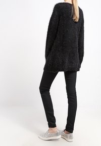 Suéter negro esponjoso, corte holgado, mangas largas, dobladillo en ángulo; combinado con pantalones negros ajustados y zapatillas plateadas. Textura suave, diseño casual.