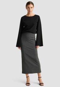 Schwarzes Oberteil mit langen, weiten Ärmeln, kombiniert mit einem eng anliegenden grauen Midirock. Das Outfit zeichnet sich durch eine schlichte Silhouette und einen sanften Stoff aus.