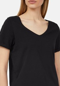 Czarna bawełniana koszulka z dekoltem w serek, krótkimi podwiniętymi rękawami i miękką fakturą. Prosty design z minimalną ilością akcentów.