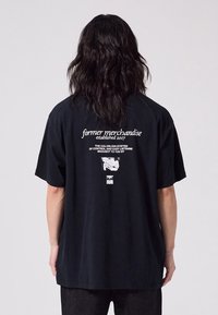 Svart bomull T-skjorte med korte ermer, med hvit tekst og grafiske trykk på baksiden. Avslappet passform og uformelt design.