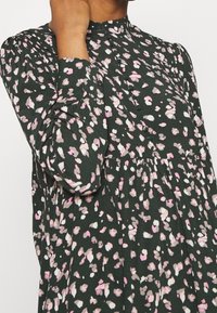 Robe imprimée florale avec un fond vert foncé agrémenté de touches roses et blanches, col montant, manches longues et détails à boutons.