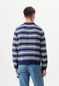 Gebreide trui in marineblauw met witte horizontale strepen. Heeft een ronde hals en geribbelde manchetten en zoom. Gedirigeerd met casual denim broek.
