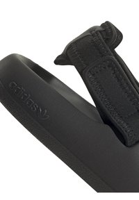 Svart Adidas flip-flop med en texturerad gummisula och ett mjukt tygband med justerbar kardborrestängning. Logotyp präglad på sidan.