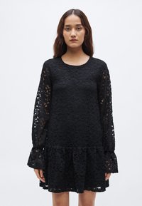 Μαύρο δαντελένιο φόρεμα με μακριά μανίκια, στρογγυλή λαιμόκοψη, φαρδιά μανσέτα και βολάν στο τελείωμα. Διαθέτει λουλουδάτα σχέδια σε όλο το ύφασμα.