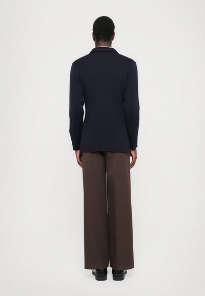 Navy knit blazer with long sleeves, notched collar, and straight cut, paired with brown wide-leg trousers and black shoes.