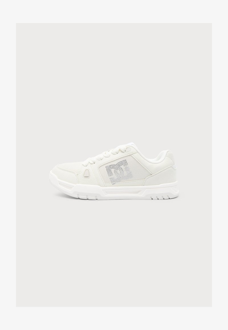 Baskets blanches à lacets, semelle texturée et panneau latéral perforé avec un logo discret sur un fond clair uni.
